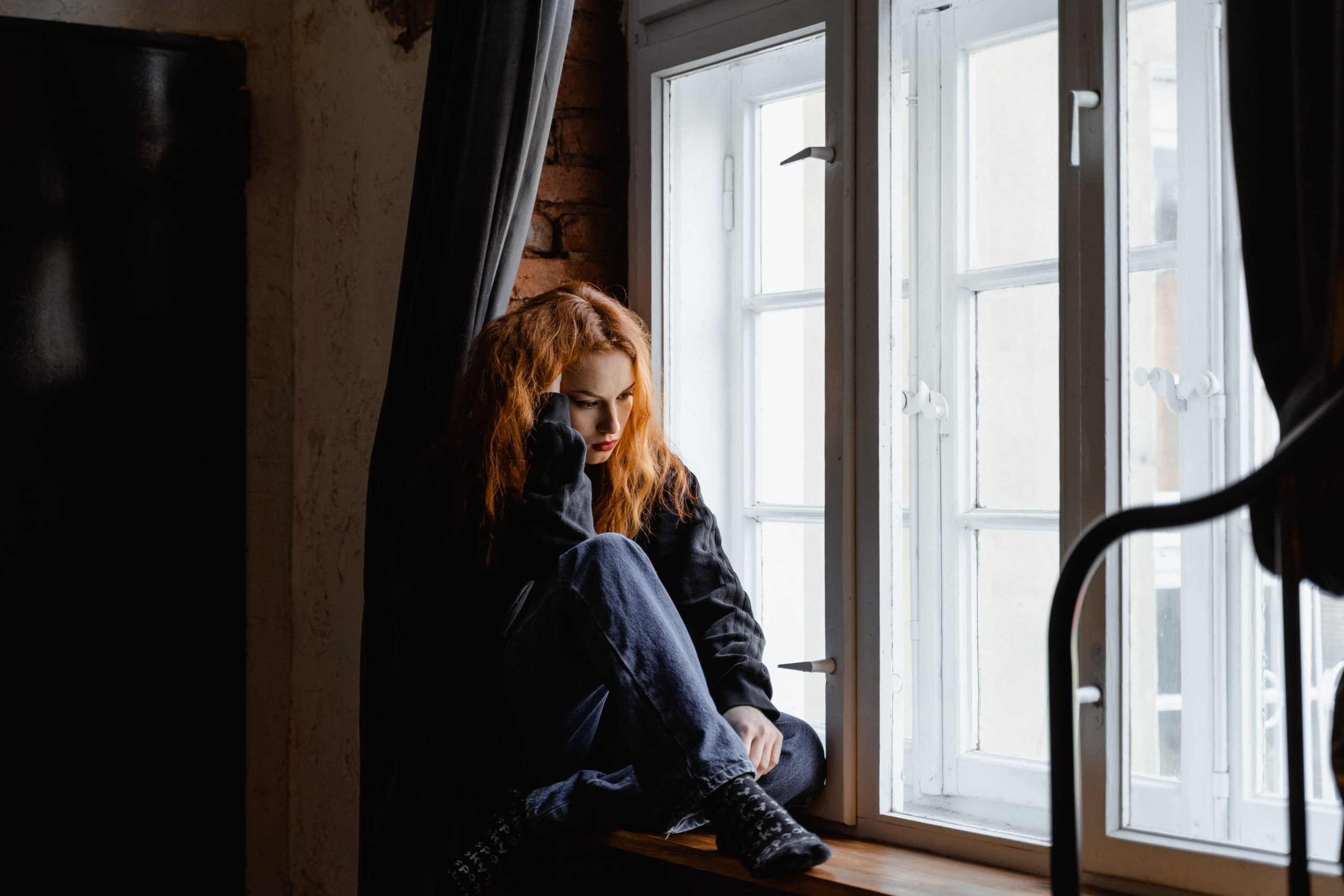 Mulher pensativa na janela pois sofre com dependência emocional